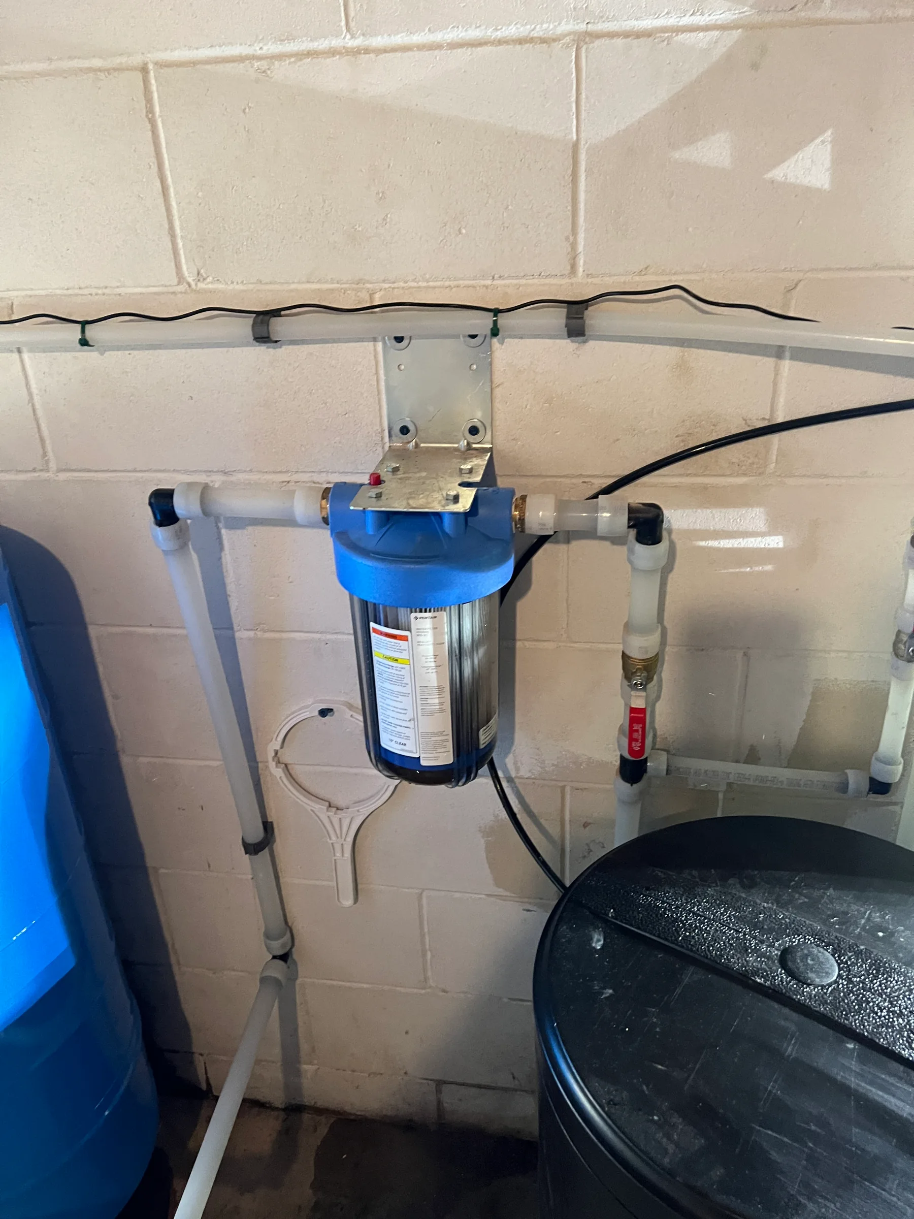 Blue water filter system mounted on beige tile wall with connected tubing and electrical cord.