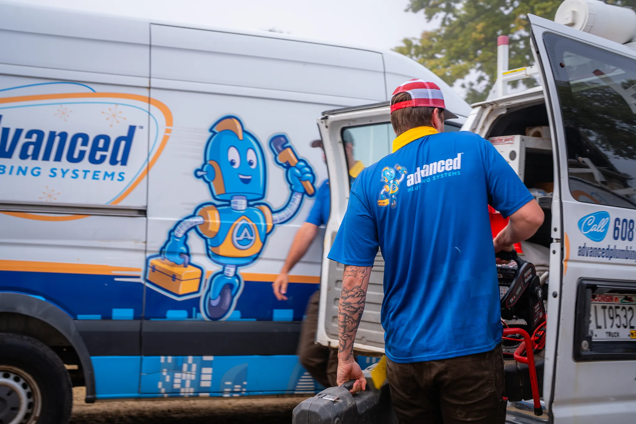 Plumber in blue Advanced Plumbing Systems shirt loading tools into service van.