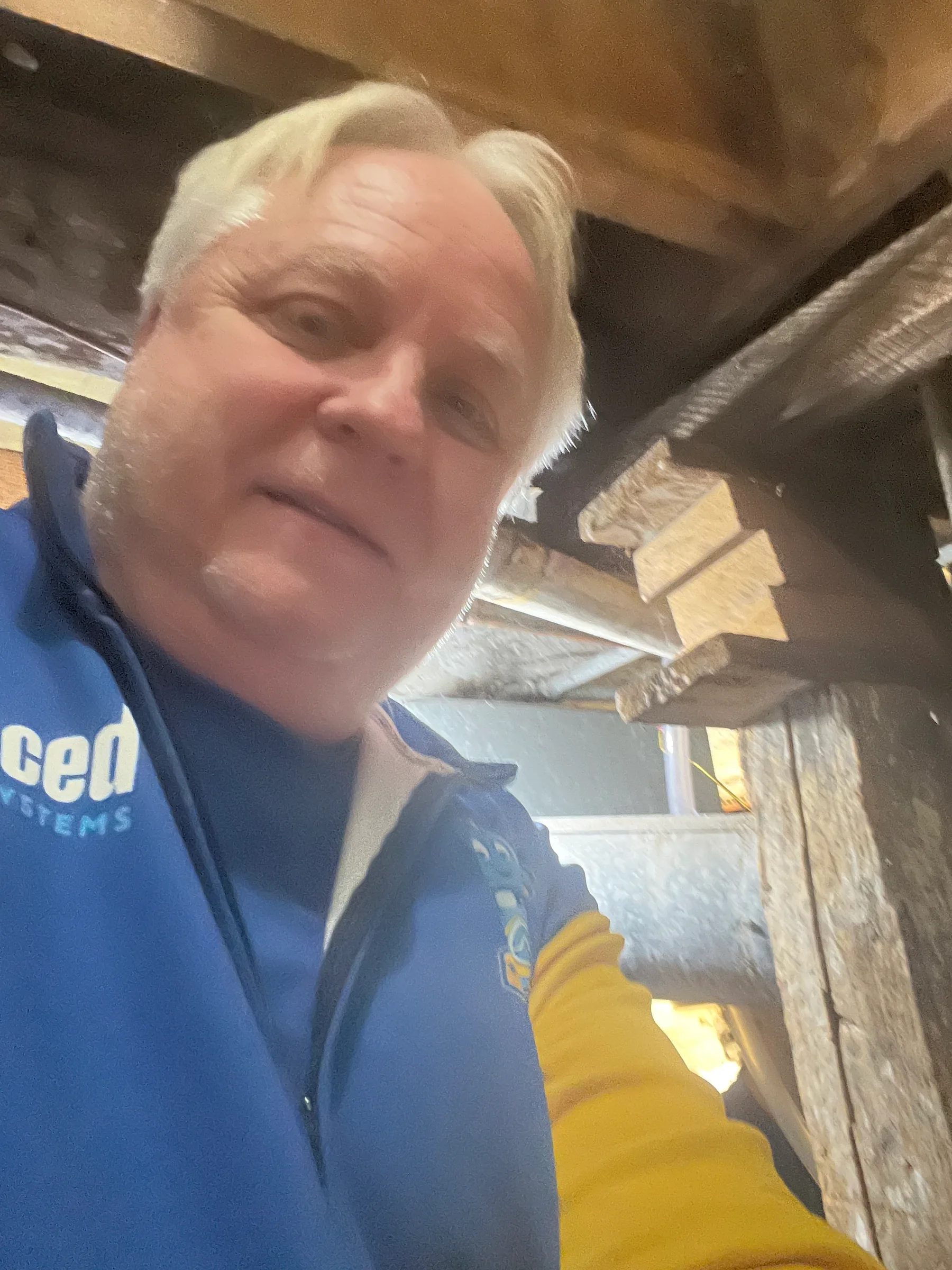 Plumber in blue uniform and yellow gloves inspecting residential plumbing work indoors.
