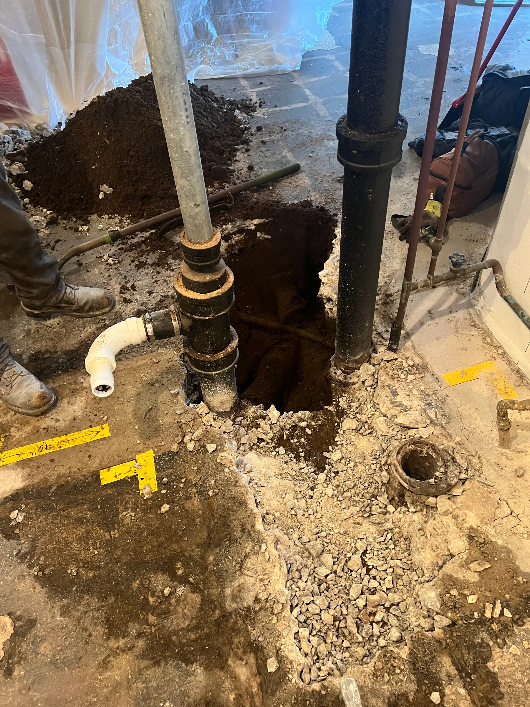 Plumber excavating underground pipes and soil during plumbing repair work with yellow measuring tape visible.