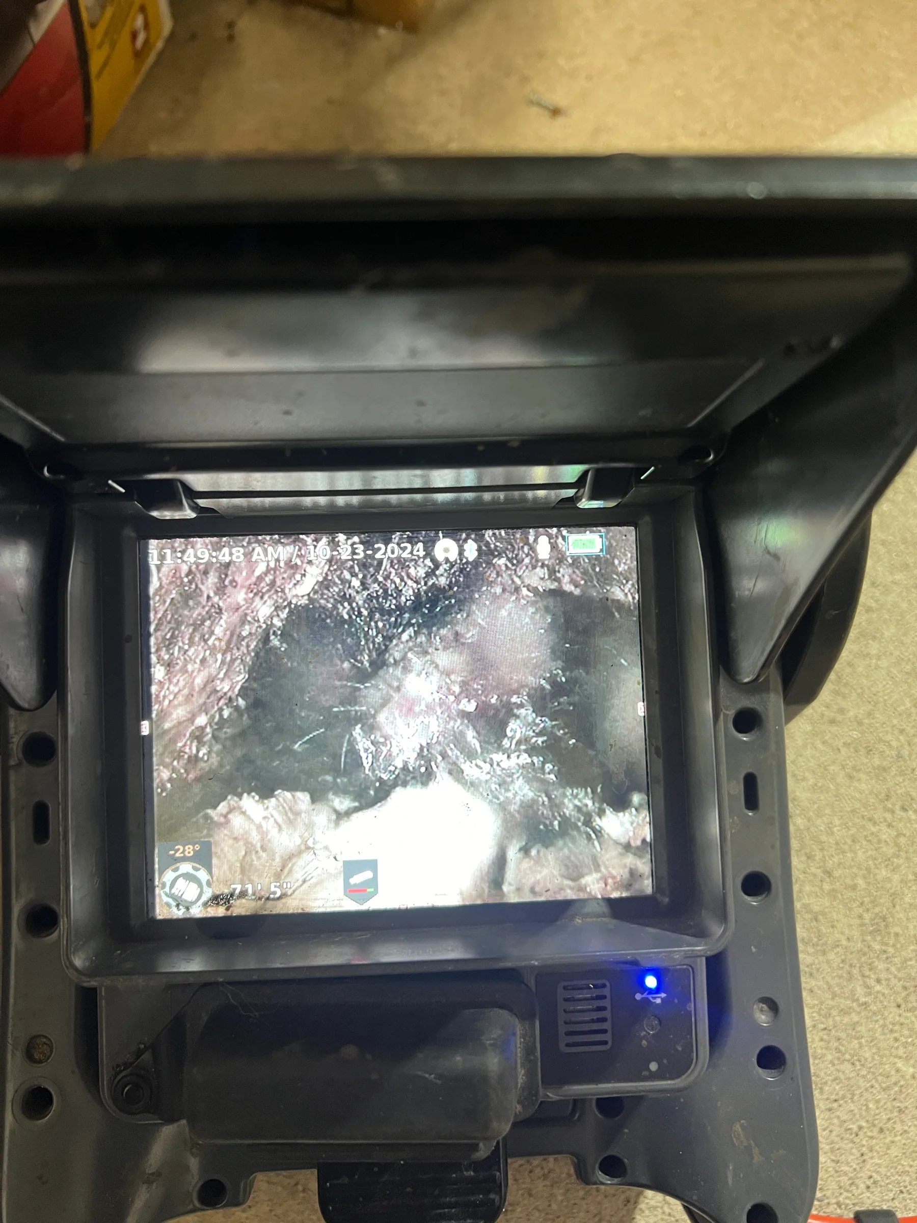 Plumbing inspection camera display showing underground pipe interior with mineral deposits and debris.
