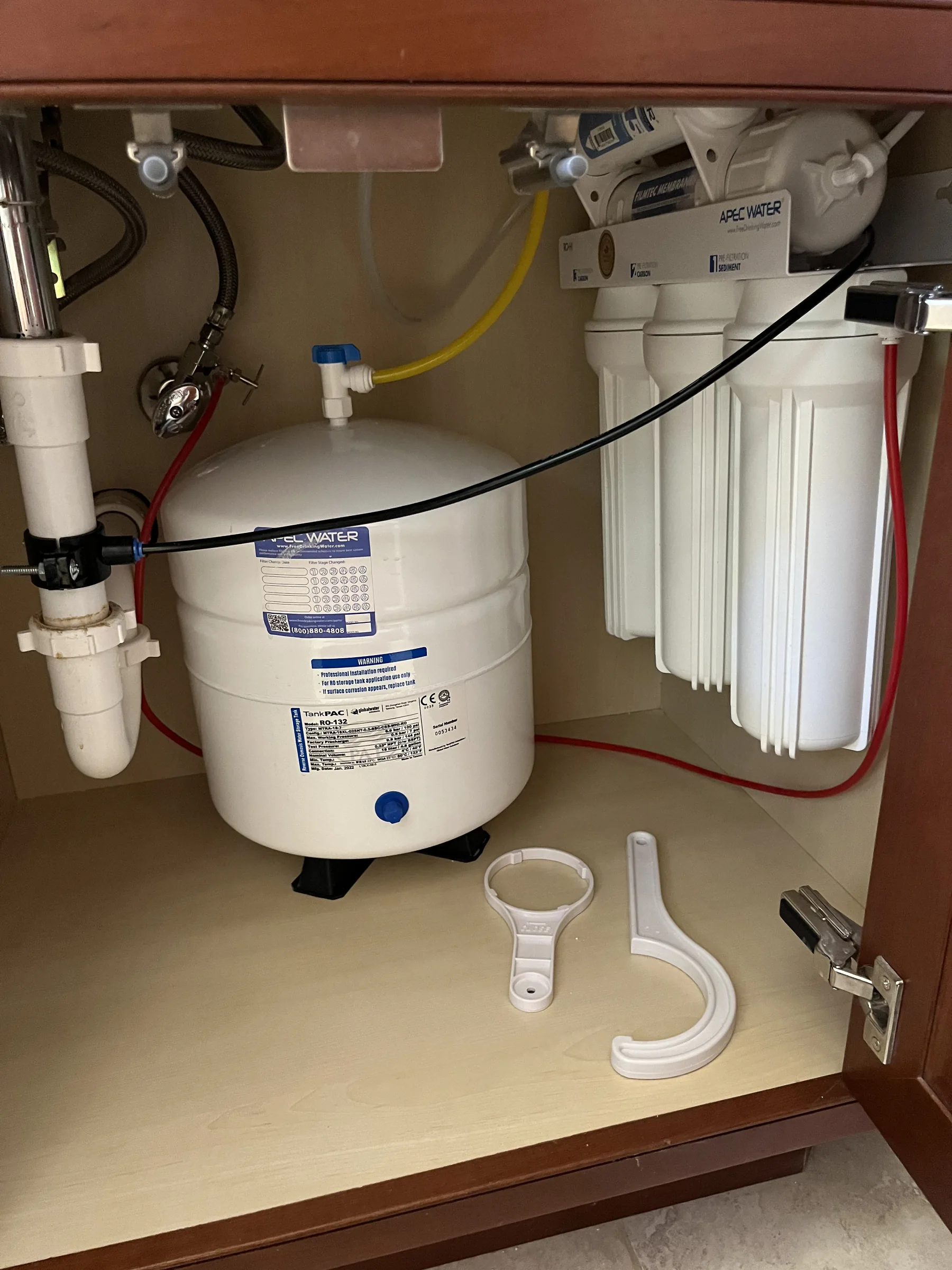 Under-sink reverse osmosis water filtration system with white storage tank and filter cartridges installed in cabinet.
