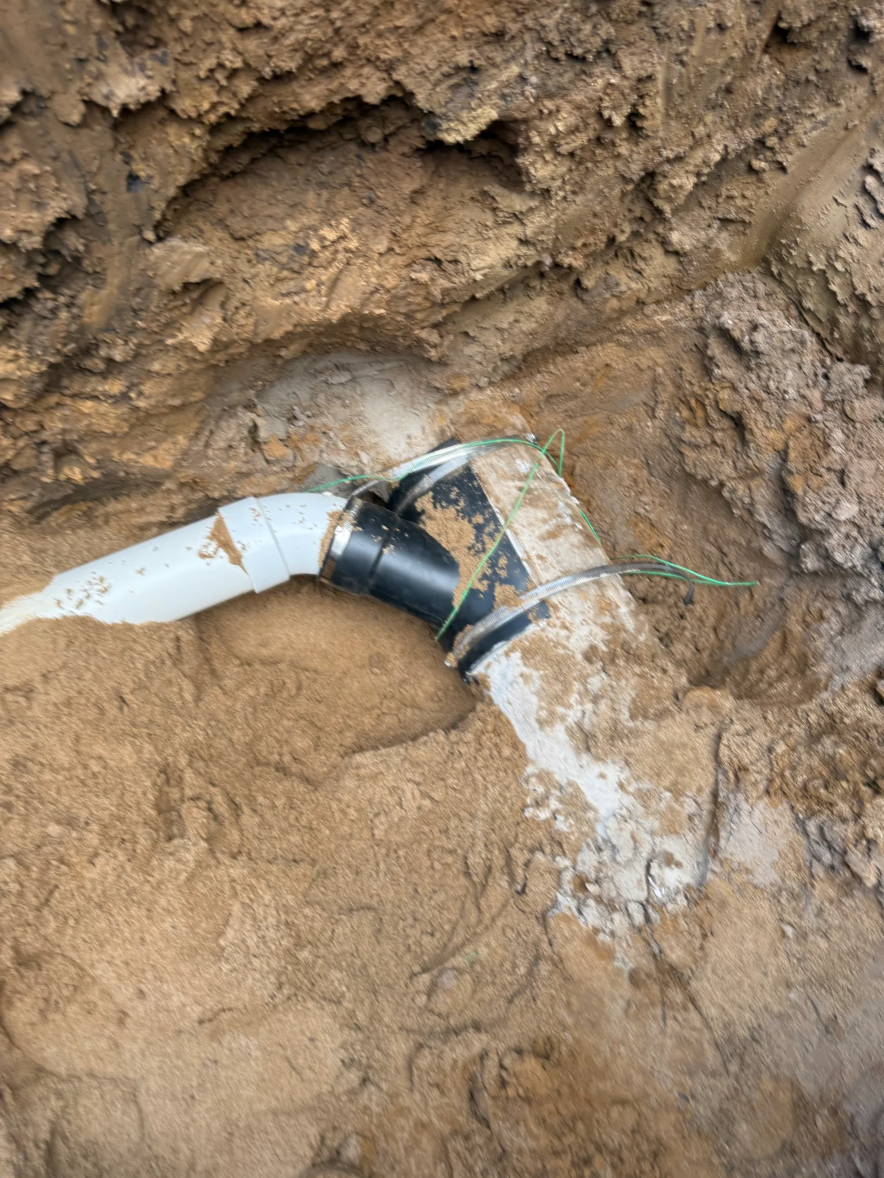 Underground water pipe with black coupling connector and green wires in excavated soil.