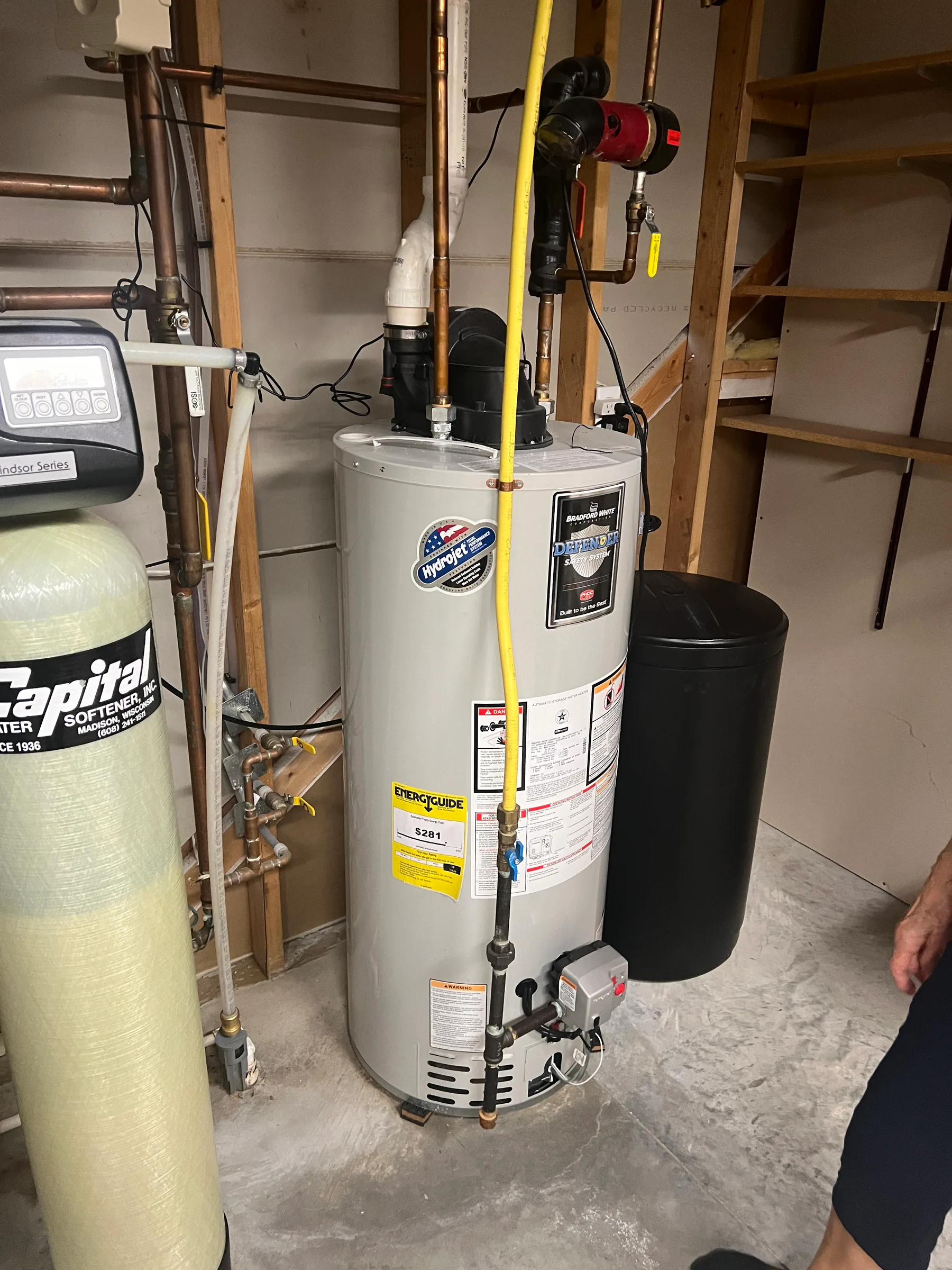 White water heater tank with yellow pipe and red pump mounted in basement utility room.